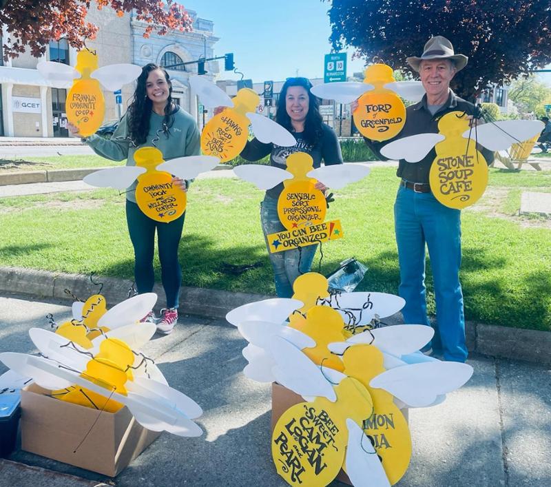 Volunteers stand holding the bee shaped lamppost signs installed every year in May